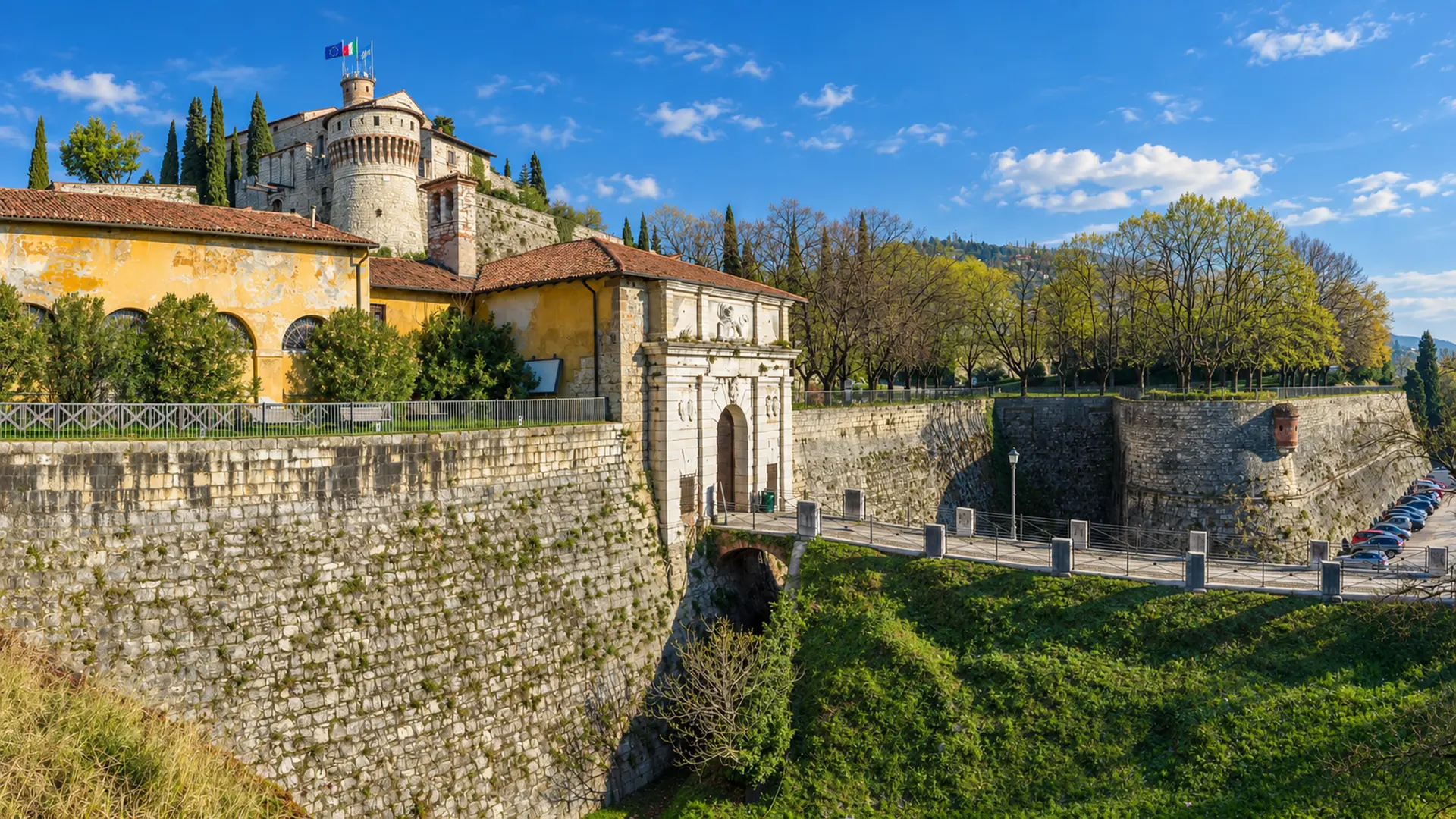 Veduta della collina fortificata con mura, ponte d'accesso e bandiere sopra Brescia, area servita dalla web agency per siti web per PMI